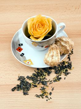 Cup of aromatic green tea with single rose and coconut cakes on wooden table