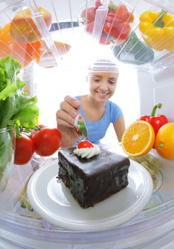 Young woman stops her diet and look for a cake in the refrigerator