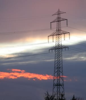 Silhouette of an electricity pylon against a cloudy winter sunset.