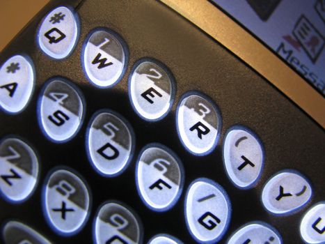 Text Messaging is a close-up shot of a PDA mobile internet communications device with backlit characters with a QWERTY keyboard.

