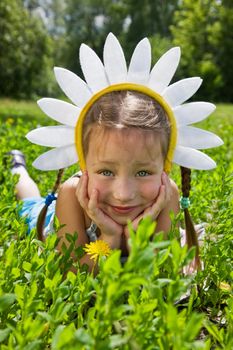 Portrait of little girl in camomile hat on green grass in a sunny day
