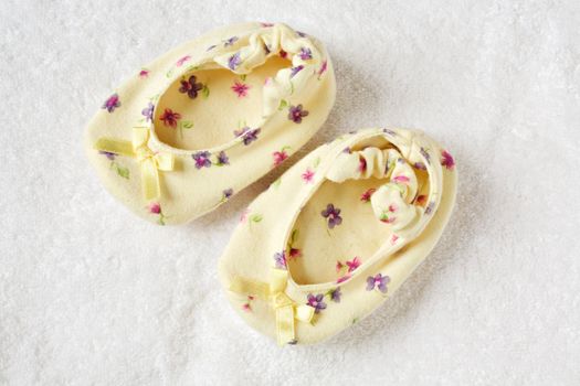 Small yellow children's bootees stand together on a white fabric
