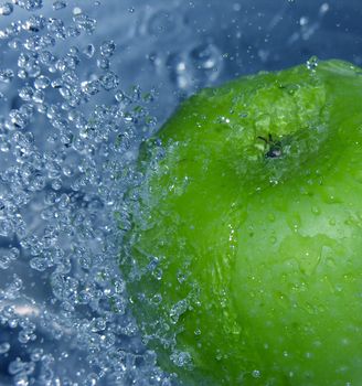 Water drops falling onto a green apple