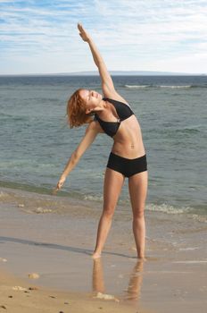 Beautiful red woman doing yoga exercises at the beach