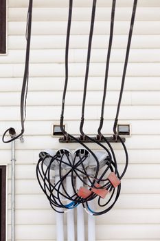 Incoming electricity supply with a complicated junction of wires and connectors on the exterior wall of a building with wooden siding