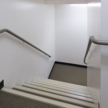 Looking down a flight of stairs in a well lit building with safety bannisters on either side