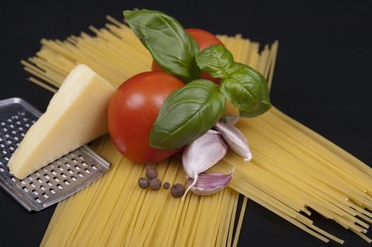 Spaghetti pasta, tomato, basil, garlic, black pepper and cheese isolated on a black background