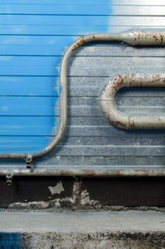 Shining steel wall with parts painted in blue color. Rusty water pipes and stone floor.