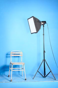 Portable studio flash (45cm x 45cm) with softbox and old chair over the blue background 