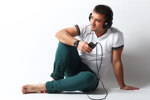 Handsome guy listening music sitting over white background