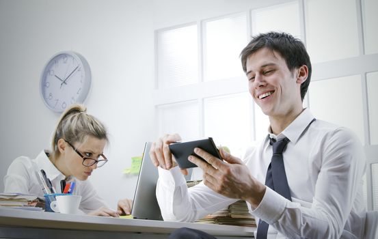 happy businessman using smart phone in office, stressed business woman on background