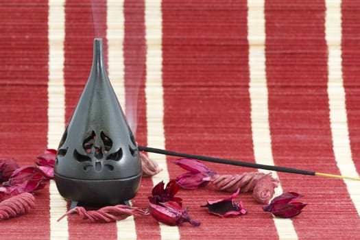 Incense stick in burner with red flower leaves 