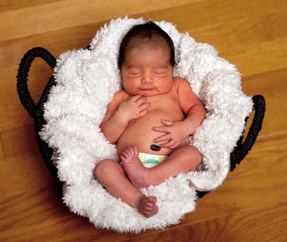 Cute baby asleep in basket with soft lining holding his belly.