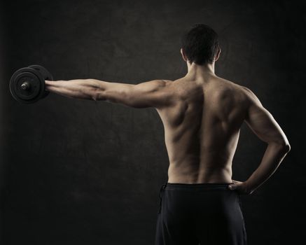 Muscular male athlete is training by lifting dumbbells