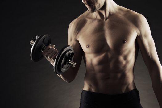 Muscular male athlete is training by lifting dumbbells