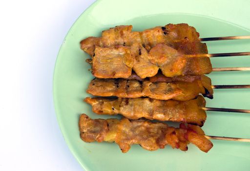 six pig skewers arranged on a green dish