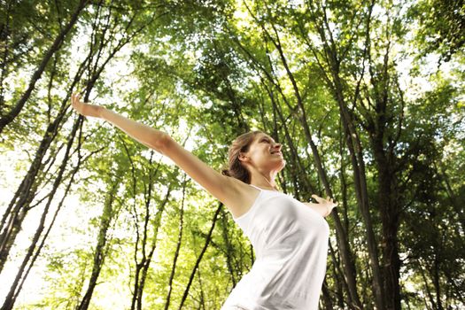 Young beautiful woman arms raised enjoying the nature in green forest