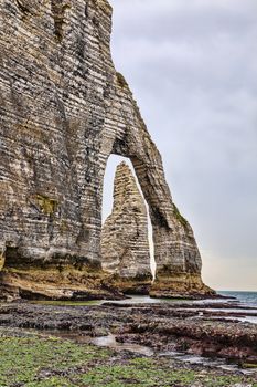 Specific cliffs in Etretat in the Upper-Normandy region in Northern France: a needle rock seen through a natural arch at the low tide time.