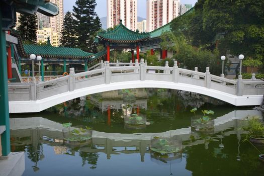 Chinese Water Garden Bridge and Reflection Amid Modern High Rise Buildings Wong Tai Sin Taoist Temple Kowloon Hong Kong