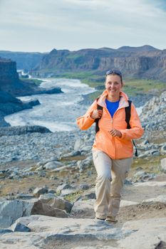 Cute woman hiking in the canyon Dettifoss waterfall in Vatnajokull National Park, Northeast Iceland. Vertical view