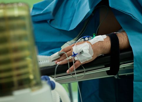 Close-up of patient's hand with drip, lying on hospital bed