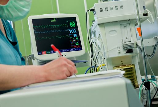Cardiogram monitor in operative room, nurse writing down information