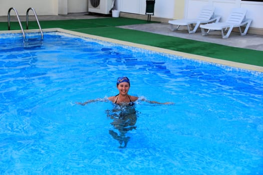 Beautiful young smiling girl sailling in pool in blue kerchief