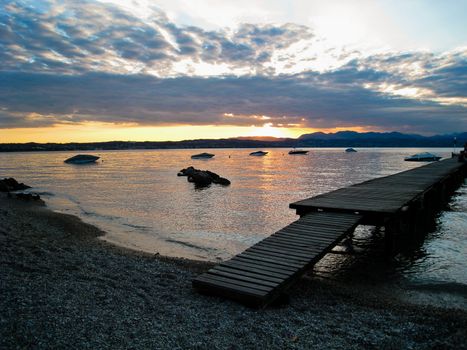 Peaceful lake with pebble beach with boats docked at a pier at dusk