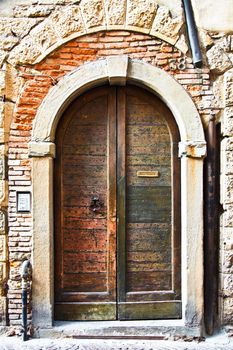 Old wooden door with a metal knocker and letter slot - wonderful texture. The door has little metal studs. On the side, there is a modern door bell and intercom. Exposed brick and pipes and a stone arch complete the picture.