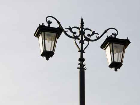 Old town street illuminator. Two lamp hangs on a metal decorative pole.