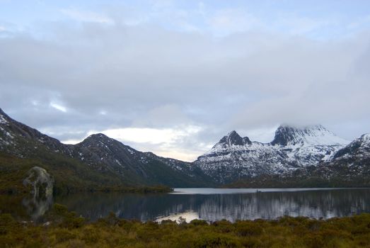 Cradle Mountain in Tasmania covered in winter snow reflected in the still water of the lake below