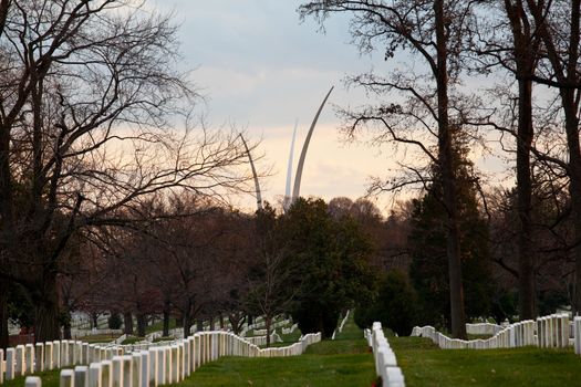 Christmas wreaths on gravestones in Arlington National Cemetery. Air Force memorial soars in the distance as the sun sets at dusk
