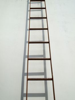 Brown iron ladder on white wall with shadow