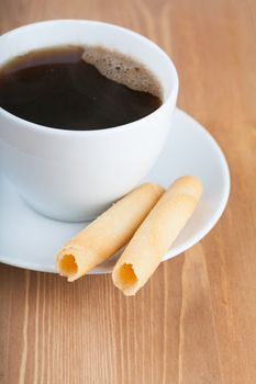 Cup of coffee with roll shaped cookies on a wooden table