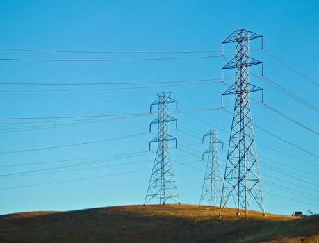 Electrical Powerlines on a Hill before a Blue Sky