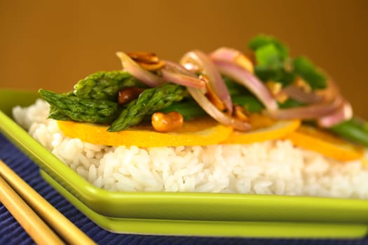 Green asparagus prepared in Thai-style with oranges, onions and peanut in an orange-ginger sauce served on rice (Selective Focus, Focus on the front of the orange slice, the two asparagus tips in the front and the peanut in the front)