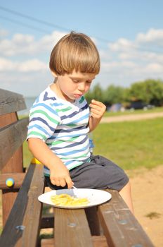 Little boy eating french fries outdoors in a beach resort