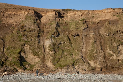 A man stands and looks up under a steep bank with areas of landslide errosion.