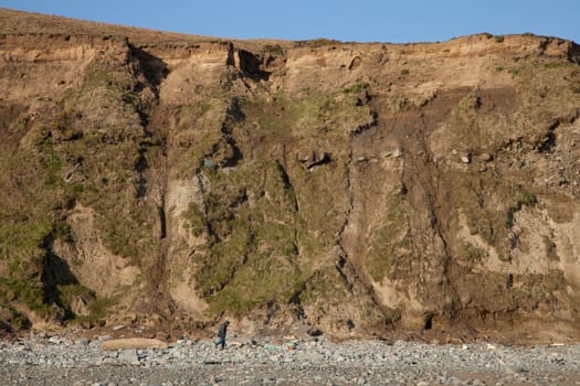 A man walks under a steep bank with areas of landslide errosion.