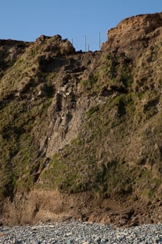 A mudslide on a pebble beach with fence posts hanging in mid air at the top.