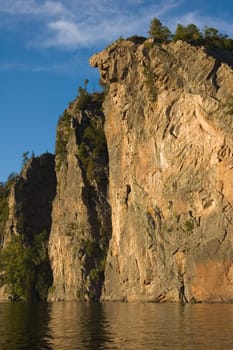 High cliff at shore of Mazinaw Lake in sunset light
