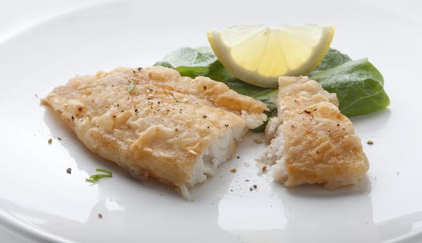 Fried fillet of tilapia with lettuce and lemon on the white plate