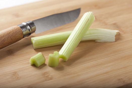 Two sticks of celery with knife on the wooden board