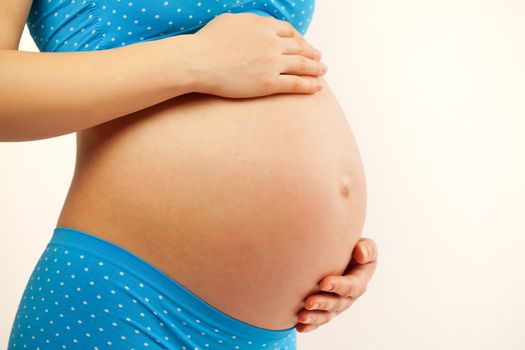 Pregnant belly with hands. Young beautiful woman during pregnancy. Blue shorts and top. 37 weeks.