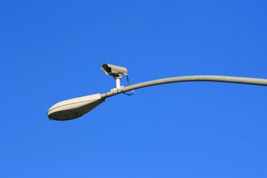 Surveillance camera on a light pole over blue sky.