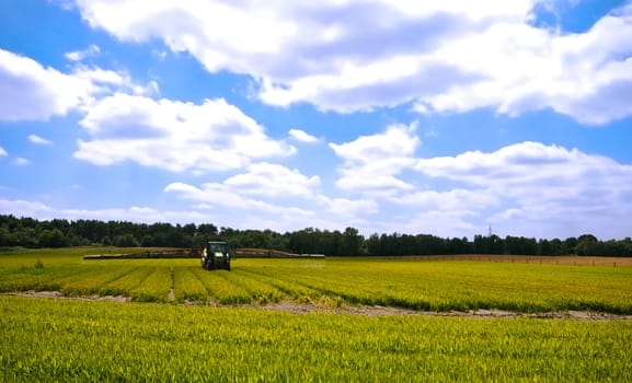 bright green agriculture farmland with tractor sprinkle-sweeper with cloudy blue sky  