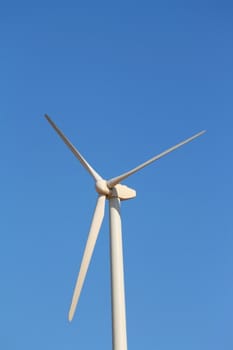 Close up of a wind turbine over blue sky.
