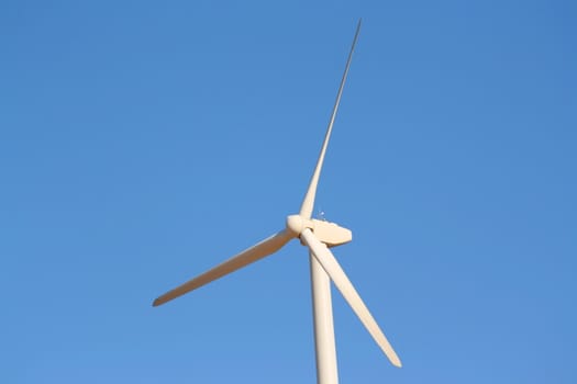 Close up of a wind turbine over blue sky.
