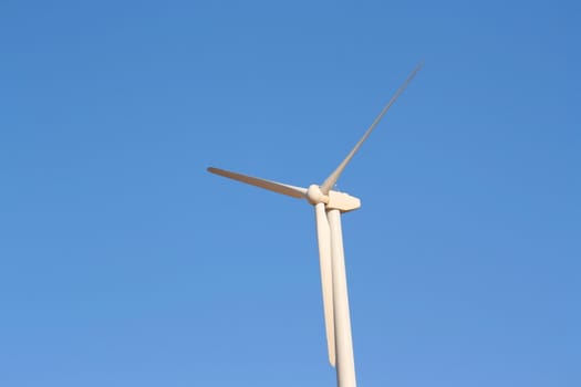 Close up of a wind turbine over blue sky.

