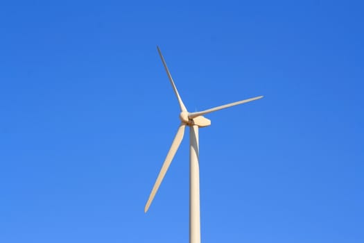 Close up of a wind turbine over blue sky.
